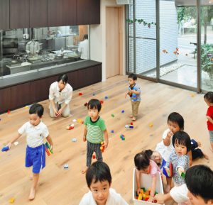 写真　吸音材が設置された天井部分（ドット状の部分）の保育室で遊ぶ子どもたち　東京都練馬区で